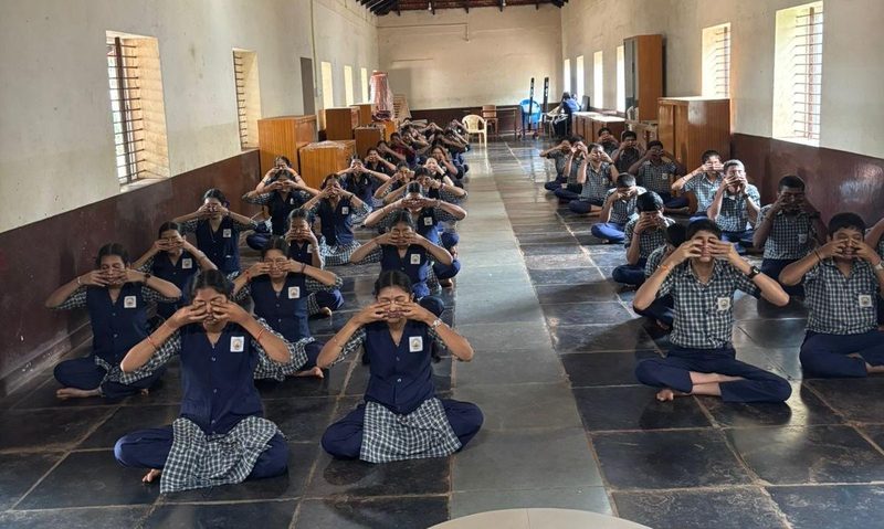 Students sitting in rows doing a breathing practice with hands at the face