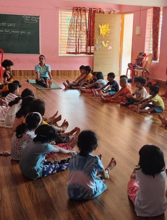 Children sitting in a circle playing a yoga game with their teacher
