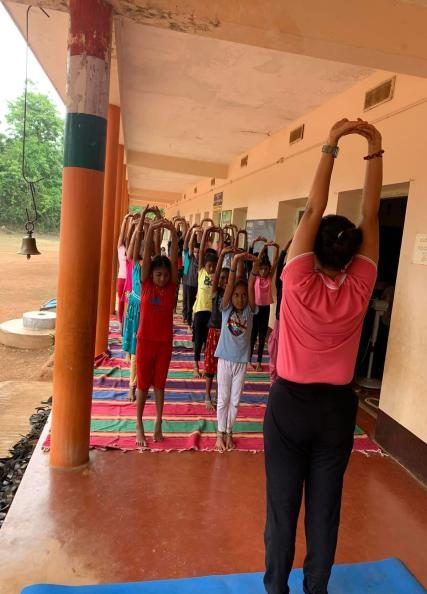 Children and teacher stretching with arms overhead on a veranda