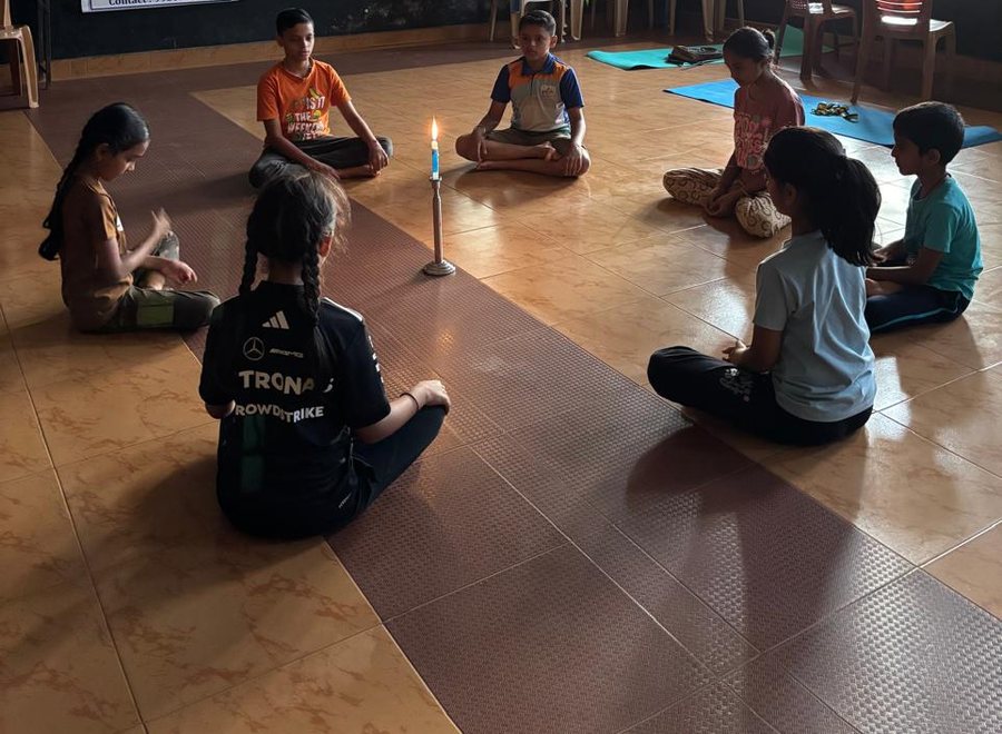 Children sitting in a circle around a lit candle during a trataka session